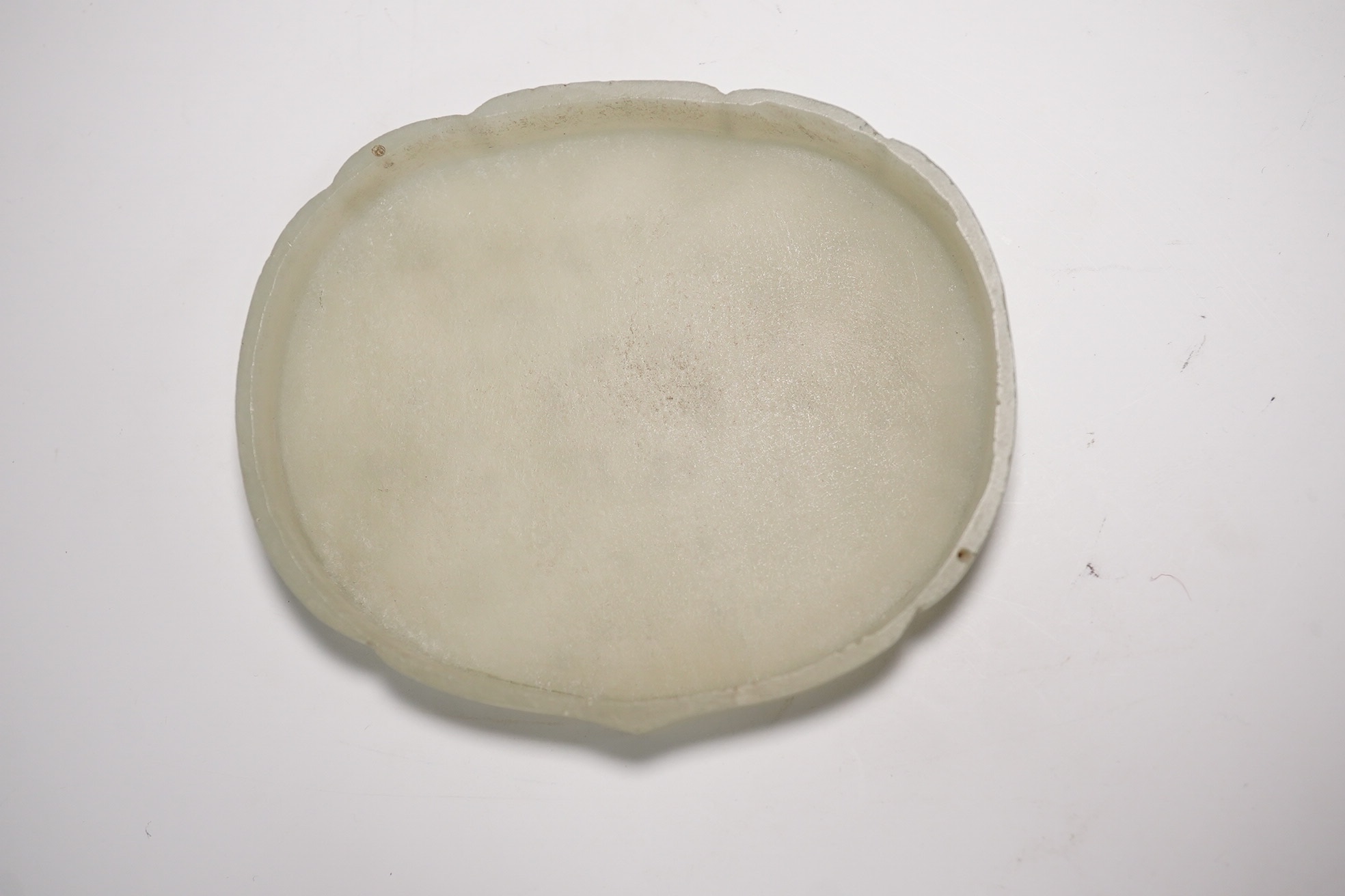 A Chinese pale celadon jade cover for a box, 19th century, carved in relief with a flaming Buddhist wheel emblem, 7.5cm wide. Condition - box base lacking, cover with feint crack